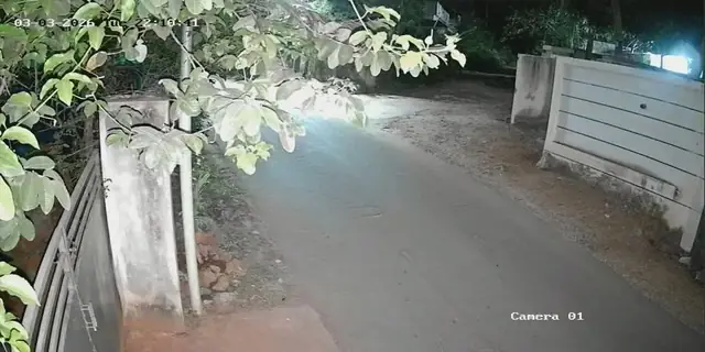 Night CCTV footage of a road and compound gate, lit by camera illumination