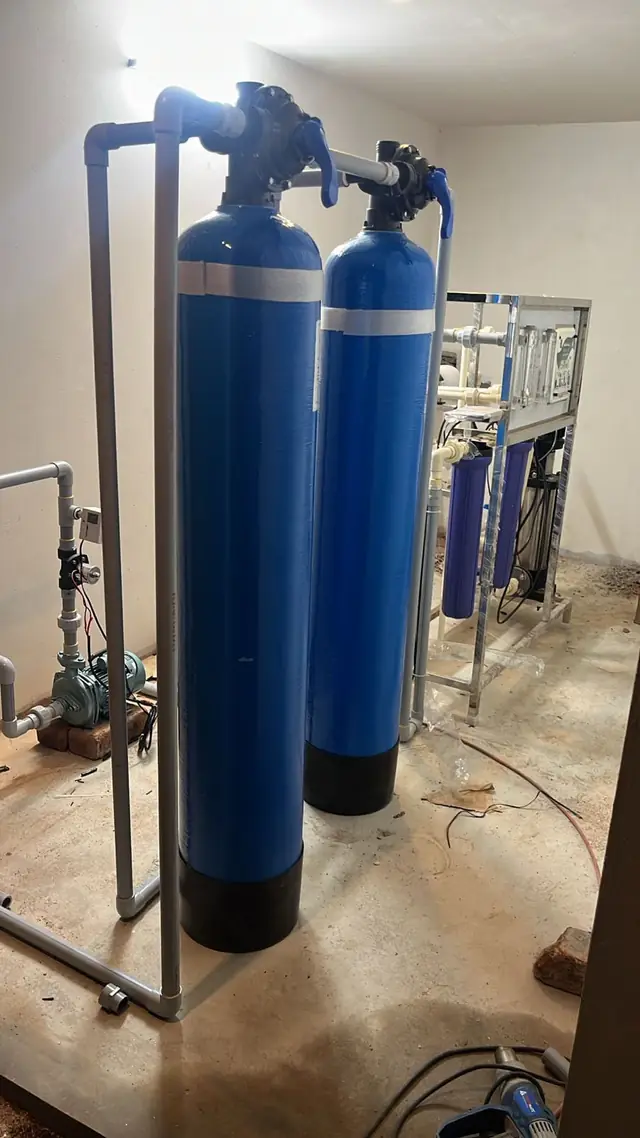 Two blue water softener vessels with valves and an RO plant behind them